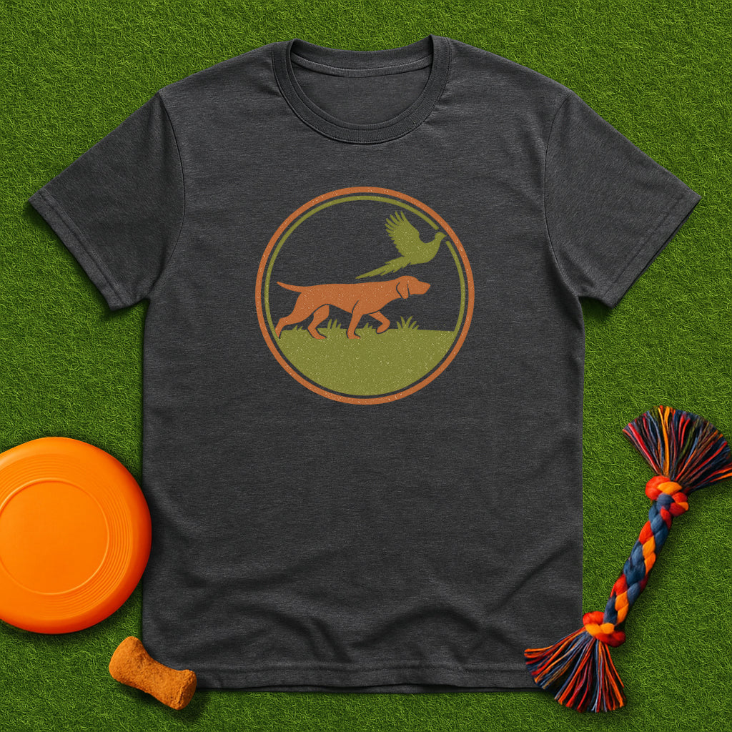 Dark gray t-shirt with a dog and bird graphic on a green surface with toys.