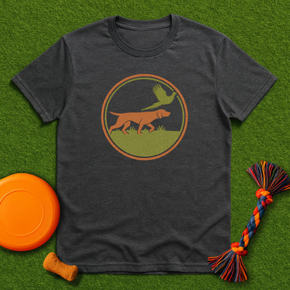 Dark gray t-shirt with a dog and bird graphic on a green surface with toys.