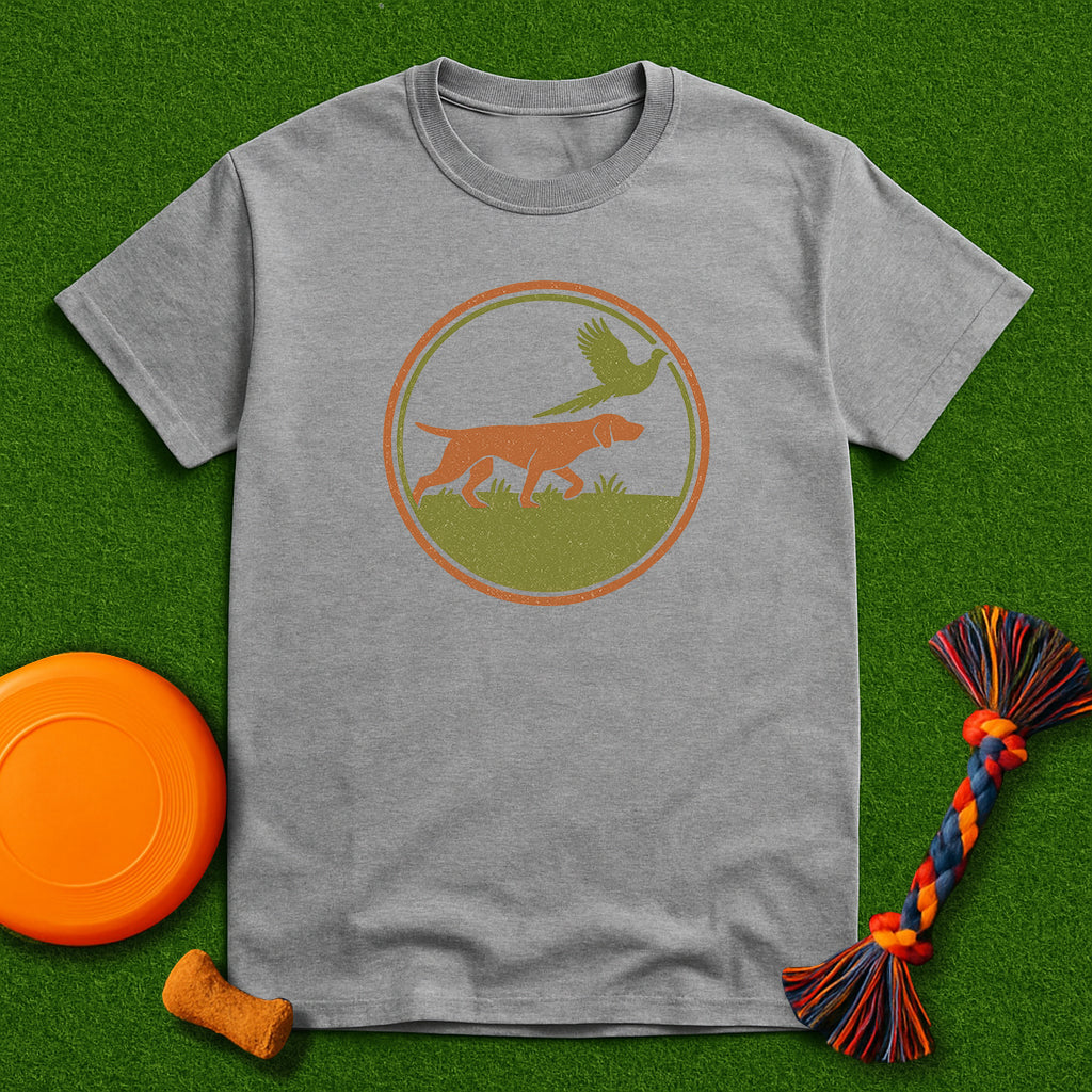 Gray t-shirt with a dog and bird graphic on a green background with a frisbee and dog toy.